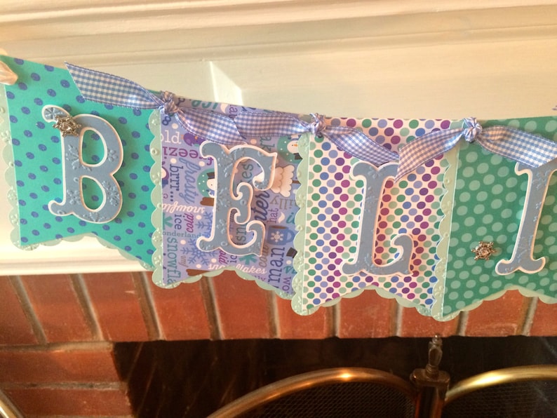 May include: A blue and green banner with white polka dots and the word "Believe" spelled out in large, blue letters. The banner is decorated with white and blue gingham ribbon.