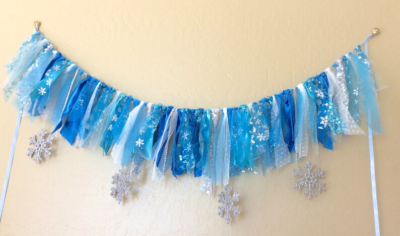 May include: A blue and white fabric banner with snowflake designs, ideal for a winter or Frozen-themed party.