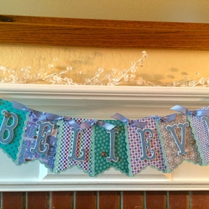 May include: A blue and white banner with the word "BELIEVE" spelled out in blue letters. The banner is decorated with snowflakes and other wintery designs.