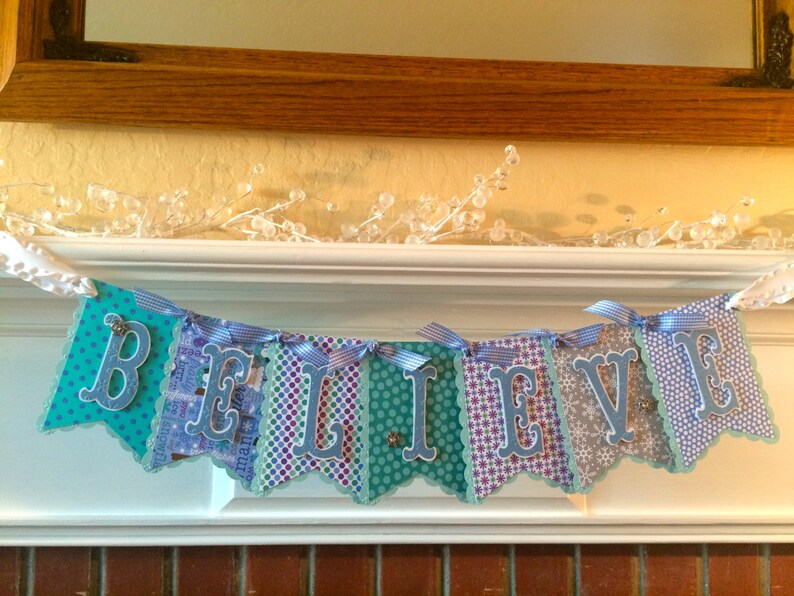 May include: A blue and white banner with the word "BELIEVE" spelled out in blue letters. The banner is decorated with snowflakes and other wintery designs.