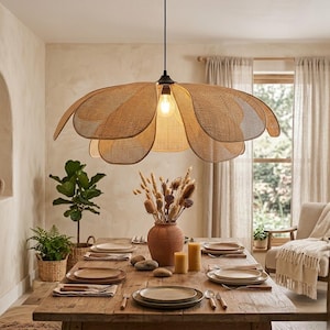 Peut inclure: Une grande suspension lumineuse dotée d'un abat-jour en rotin tressé en forme de fleur épanouie avec plusieurs pétales superposés. La lampe est suspendue par un cordon et une douille noirs, éclairant une table à manger d'une lueur douce.