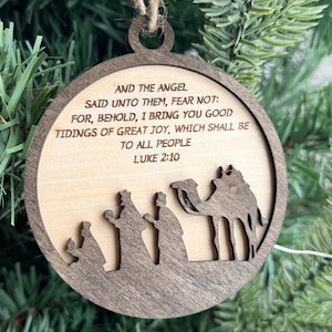 May include: A round wooden Christmas ornament featuring a dark brown frame and a light wood center. The text reads: AND THE ANGEL SAID UNTO THEM, FEAR NOT: FOR, BEHOLD, I BRING YOU GOOD TIDINGS OF GREAT JOY, WHICH SHALL BE TO ALL PEOPLE LUKE 2:10.