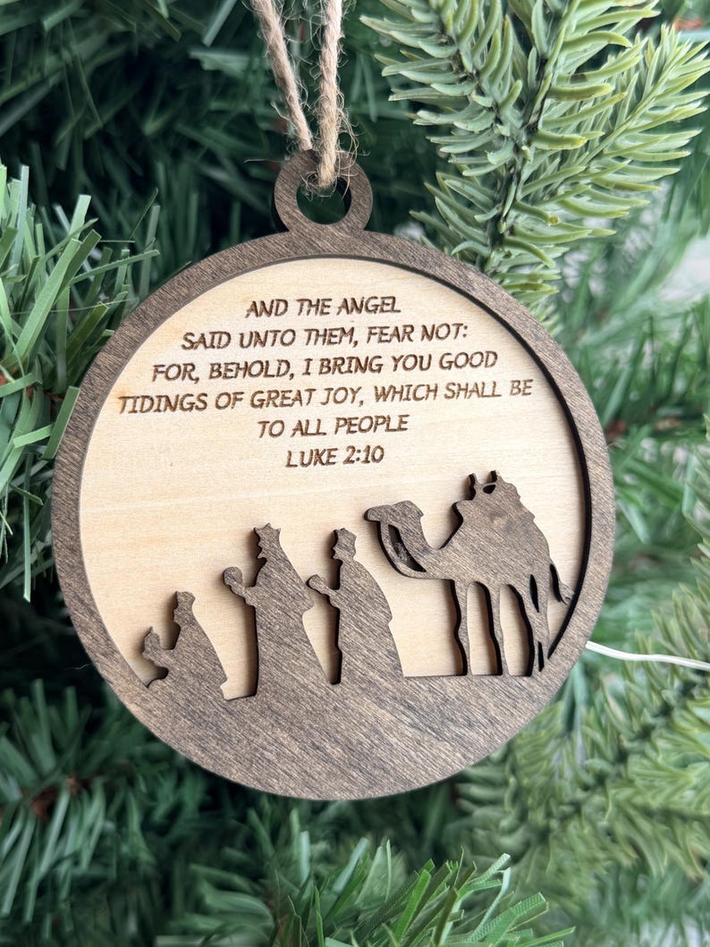 May include: A round wooden Christmas ornament featuring a dark brown frame and a light wood center. The text reads: AND THE ANGEL SAID UNTO THEM, FEAR NOT: FOR, BEHOLD, I BRING YOU GOOD TIDINGS OF GREAT JOY, WHICH SHALL BE TO ALL PEOPLE LUKE 2:10.