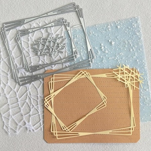 Pode incluir: Um conjunto de matrizes de corte em metal prateado com molduras retangulares encaixadas, detalhes geométricos nos cantos e um design central de linhas cruzadas. As matrizes estão dispostas sobre uma superfície clara com padrão de renda.