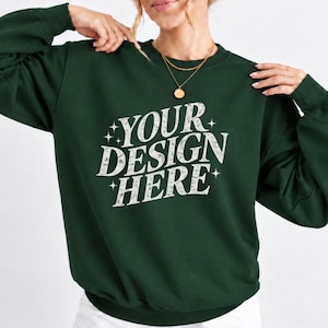 May include: A dark forest green long-sleeve crewneck sweatshirt featuring the white distressed text "YOUR DESIGN HERE" centered on the chest, accented by small four-pointed star graphics. The garment has ribbed cuffs and a ribbed hemline.