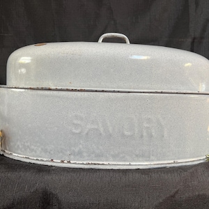 May include: A vintage, light gray enamelware roaster with a lid and handles. The word "SAVORY" is embossed on the side. The roaster has a speckled finish and a rustic, aged appearance, suggesting it's an antique kitchenware item.