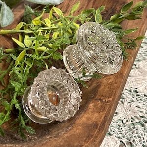 May include: Two clear glass cabinet knobs with a diamond pattern on a wooden surface.