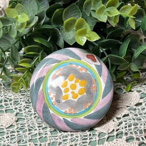 May include: A round ceramic knob with a swirl pattern in shades of pink, green, and gray. The center of the knob features a yellow and gray flower design with white dots.