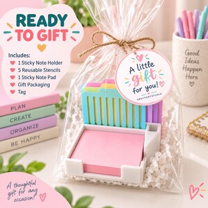 May include: A white plastic sticky note holder containing a pink sticky note pad and five colorful plastic stencils. The set is wrapped in clear cellophane with a brown twine bow and a round tag that reads A little gift for you! KRAFTORYSTUDIO.
