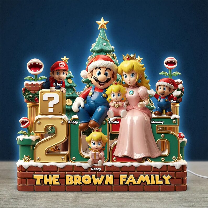 Może przedstawiać: Dekoracyjna ozdoba świąteczna z motywem Super Mario, przedstawiająca figurki Mario, księżniczki Peach i dzieci. Podstawa zawiera napis THE BROWN FAMILY oraz rok 2025. Postacie są podpisane imionami takimi jak Brian, Daddy, Amelia, Mommy, Kevin i Nancy.