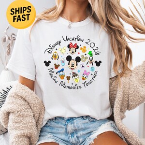 May include: A white short-sleeve t-shirt featuring a circular graphic with the text Disney Vacation 2020 Making Memories Together. The design includes colorful illustrations of Mickey Mouse, Minnie Mouse, Donald Duck, Daisy Duck, Goofy, and Pluto.