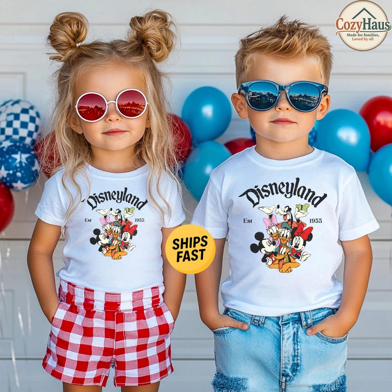 K&ouml;nnte beinhalten: Zwei Kinder tragen wei&szlig;e T-Shirts mit einem Disneyland Est 1955-Aufdruck, der Mickey Maus, Minnie Maus, Donald Duck, Daisy Duck, Goofy und Pluto zeigt. Ein Kind tr&auml;gt rot-wei&szlig; karierte Shorts, das andere eine blaue Jeanshose.