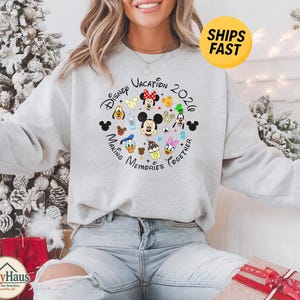 May include: A light gray crewneck sweatshirt featuring a circular graphic with various Disney character faces, including Mickey Mouse, Minnie Mouse, Donald Duck, and Goofy, with the text Disney Vacation 2020 Making Memories Together.