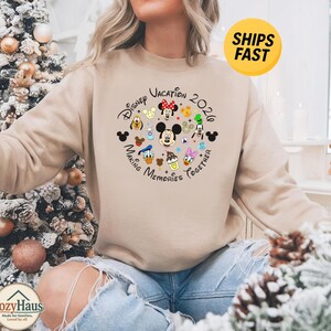 May include: A beige crewneck sweatshirt featuring a circular graphic with Disney character faces including Mickey, Minnie, Donald, Daisy, Goofy, and Pluto, with the text Disney Vacation 2020 Making Memories Together printed in black lettering.
