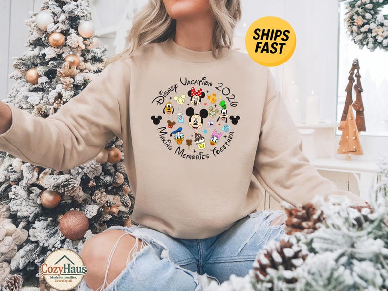 May include: A beige crewneck sweatshirt featuring a circular graphic with Disney character faces including Mickey, Minnie, Donald, Daisy, Goofy, and Pluto, with the text Disney Vacation 2020 Making Memories Together printed in black lettering.