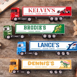 Peut inclure: Quatre camions jouets avec remorques. Le camion rouge indique KELVIN'S TRUCKING COMPANY avec une voiture de course. Le vert indique BRODIE'S TRUCKING COMPANY avec un ballon de football. Le bleu indique LANCE'S TRUCKING COMPANY avec un requin. Le jaune indique DENNIS'S TRUCKING COMPANY avec un dinosaure.