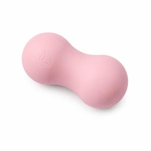 Peut inclure: Une balle de massage rose clair en forme de cacahuète avec une texture lisse et mate. L'objet présente un design à deux sphères reliées par un centre étroit, avec un petit logo circulaire en relief visible sur l'une des extrémités arrondies.