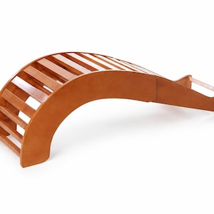 Peut inclure: Un étireur de dos en bois courbé composé d'une série de lattes parallèles formant une arche. La structure présente une finition lisse et polie dans une teinte brun chaud, avec une extension plate à une extrémité et une base solide.