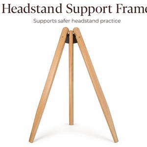 May include: A light brown wooden headstand support frame with three legs connected at the top by a dark circular joint. The text Headstand Support Frame and Supports safer headstand practice is printed in dark brown above the wooden structure.
