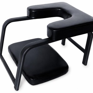 May include: A black massage chair featuring a U-shaped headrest and a separate rectangular seat cushion. The frame is constructed from black metal tubing, supporting the padded headrest and the lower seat section in a tiered, open design.