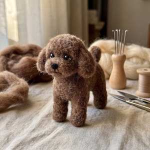 May include: A needle-felted brown poodle figurine with curly wool texture, dark bead eyes, and a small black nose. The sculpture stands upright, featuring floppy ears and a short tail, crafted from brown wool fibers with a soft, fuzzy appearance.
