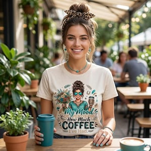 Pode incluir: Uma t-shirt de manga curta cor de creme com um gráfico de uma pessoa com um coque desarrumado e uma fita de cabeça com padrão de leopardo, segurando um ramo de flores e um copo de café, com o texto My Mood Depends On How Much Coffee I've Had.
