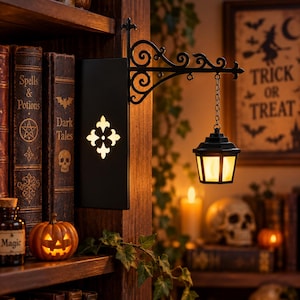May include: A black metal wall-mounted lantern fixture featuring an ornate scrollwork bracket and a hanging lantern with a warm glowing light. The rectangular base plate displays a cutout fleur-de-lis design that emits a soft, internal illumination.