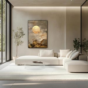 May include: A rectangular wall art piece featuring an abstract painting of a glowing golden moon set against a textured, dark gray and brown cloudy sky. The artwork is framed in a thin black border and hangs above a large, white sectional sofa.