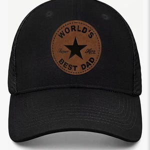 Può includere: Cappellino da baseball nero con toppa in pelle marrone. La toppa presenta una stella nera e le parole "WORLD'S BEST DAD" in un design circolare. Il testo "Super" e "Here" è incluso sulla toppa.