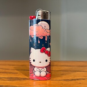 May include: A decorative lighter with a Hello Kitty design. The lighter has a blue background with a pink cloud and moon graphic at the top. The bottom of the lighter features a Hello Kitty character with a red bow.
