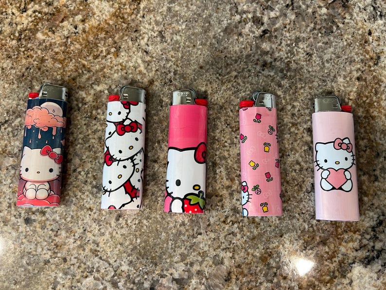May include: Five Hello Kitty-themed lighters with different designs. One shows a rainy cloud, another has repeating bows, and others feature Hello Kitty with a strawberry, flowers, and a heart. Each lighter has a silver metal top.
