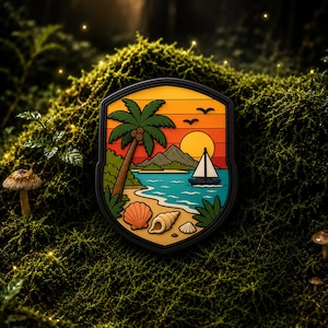 Op de afbeelding: Een schildvormige patch met een tropisch strandtafereel, een palmboom, een zeilboot op blauw water, bergen en een zonsondergang. Op de voorgrond liggen drie schelpen op een zandstrand, omlijst door een dikke zwarte rand.