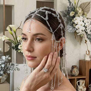 May include: A decorative headpiece constructed from a network of thin silver-toned chains and clear, spherical glass beads. The accessory features multiple dangling strands that drape over the sides, accented with teardrop-shaped crystal pendants.
