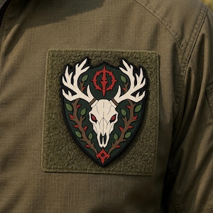 May include: A shield-shaped patch featuring a white deer skull with large antlers, set against a dark green background. The design includes brown thorny branches with green leaves and a red circular emblem at the top, all bordered in black.