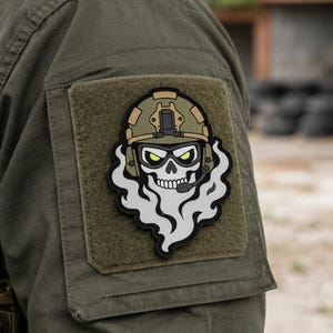 May include: A tactical morale patch featuring a stylized skull wearing an olive drab combat helmet, tactical goggles with glowing yellow eyes, and a communication headset, with a thick grey smoke cloud billowing from the base of the skull.