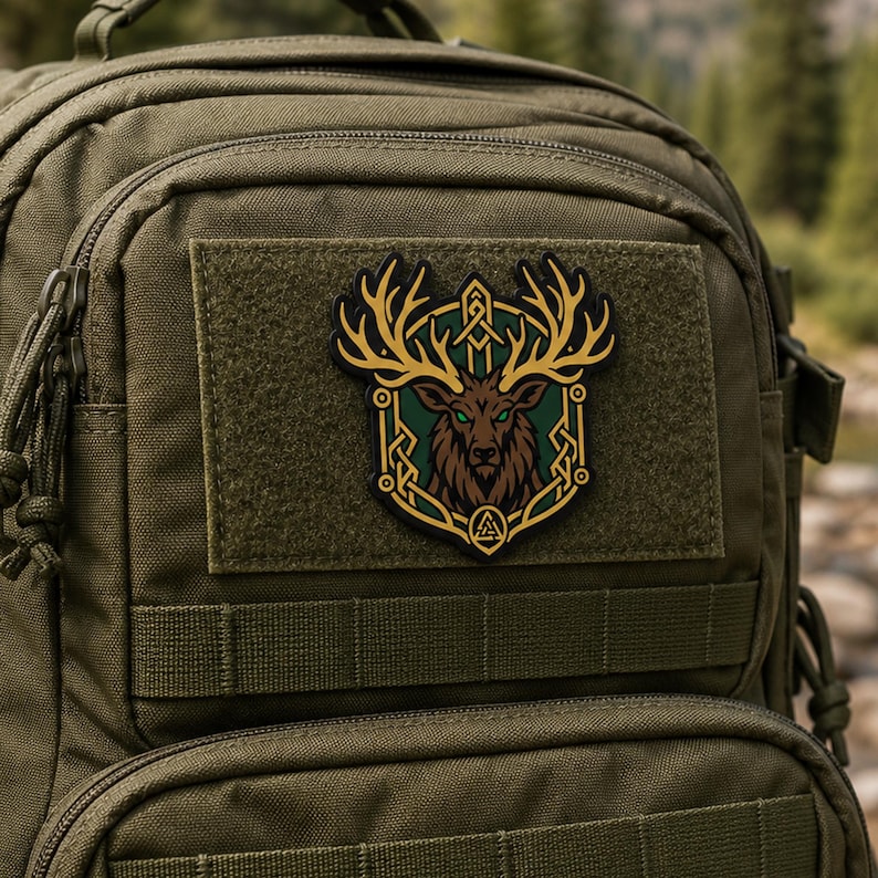 May include: An olive green tactical backpack featuring a rectangular patch with a brown deer head illustration. The deer has large antlers, glowing green eyes, and is framed by a gold-colored border with intricate knotwork and a small triangle symbol.