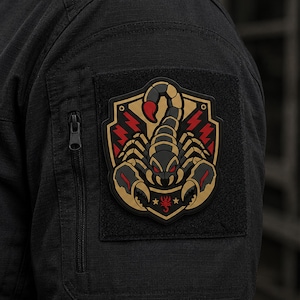 May include: A black tactical patch featuring a stylised scorpion design in gold, black, and red. The scorpion is centred on a shield-shaped emblem with red lightning bolt accents on both sides and a small red scorpion icon at the bottom base.