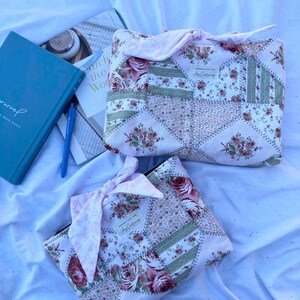 May include: Two rectangular fabric pouches featuring a patchwork design of pink roses, green stripes, and small floral patterns. Each pouch has a tied fabric bow closure at the top and a small white label with the text Any Contrivance sewn on the front.