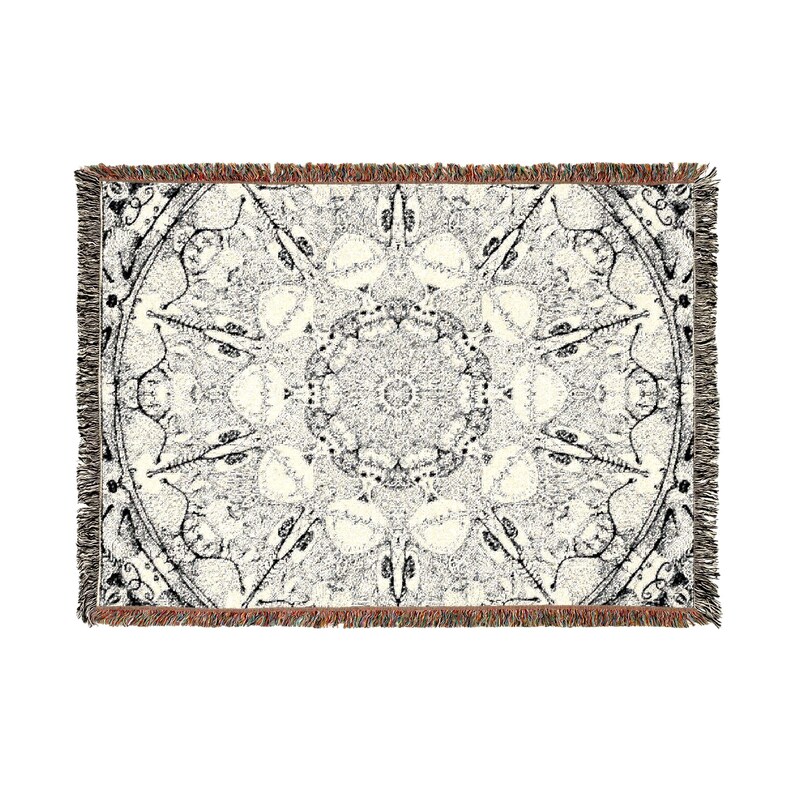 Peut inclure: Un plaid tiss&eacute; rectangulaire pr&eacute;sentant un motif complexe inspir&eacute; d'un mandala en noir et blanc. Le design se compose de formes g&eacute;om&eacute;triques sym&eacute;triques et de lignes fines rayonnant depuis un point central, avec des bords &agrave; franges.