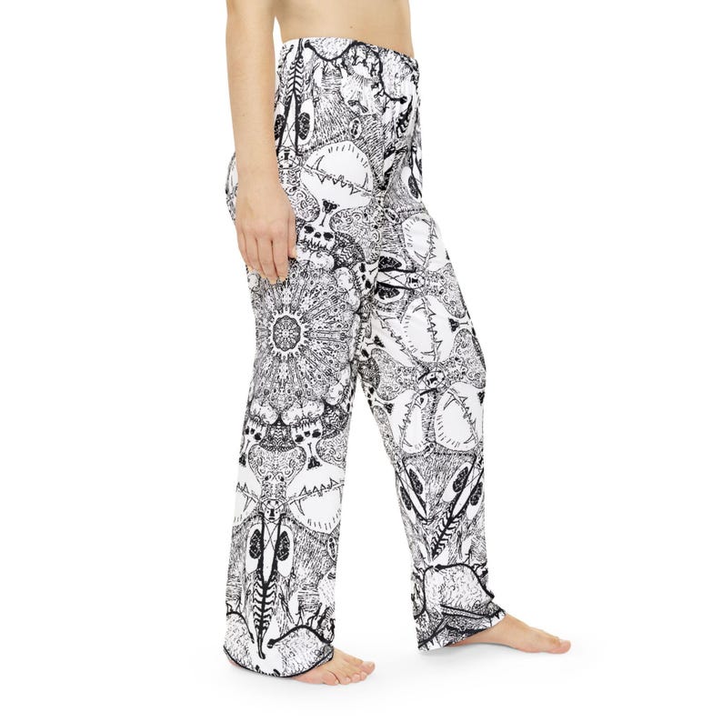 K&ouml;nnte beinhalten: Lange Freizeithose mit einem kontrastreichen, schwarz-wei&szlig;en, komplexen Grafikmuster. Das Design zeigt sich wiederholende Illustrationen von Totenk&ouml;pfen, Skelettstrukturen und mandalaartigen kreisf&ouml;rmigen Motiven, die auf die gesamte Stoffoberfl&auml;che gedruckt sind.