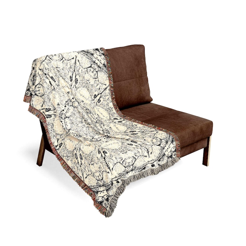 Peut inclure: Un plaid tiss&eacute; pr&eacute;sentant un motif botanique cr&egrave;me et noir avec des illustrations complexes de feuilles et de vignes. Le textile rectangulaire poss&egrave;de une surface textur&eacute;e et des bords finis avec des d&eacute;tails de franges effiloch&eacute;es.