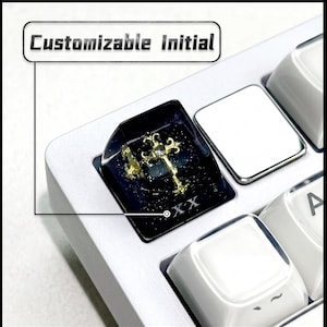 May include: A black resin mechanical keyboard keycap featuring a gold-coloured cross emblem with a central clear stone, embedded glitter, and the Roman numeral XX at the base. A text box above the keycap displays the words Customizable Initial.