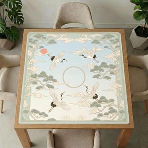 Cranes and pine clouds mahjong mat covering a square wooden dining table, surrounded by neutral upholstered chairs and green indoor plants.