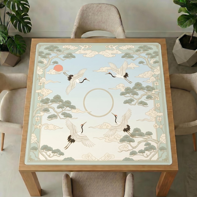 Cranes and pine clouds mahjong mat covering a square wooden dining table, surrounded by neutral upholstered chairs and green indoor plants.