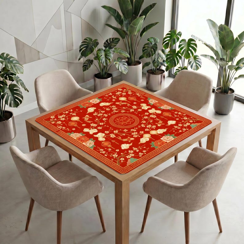Red lantern koi lotus mahjong mat displayed on a square table in a bright modern room, styled with soft chairs and tall potted plants.