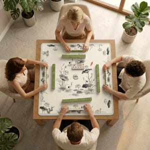 Top‑down view of four people sitting around a table covered with the ink crane lotus mahjong table mat, preparing to play mahjong.