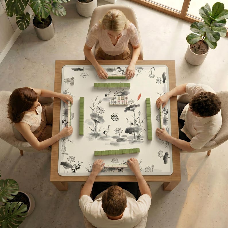 Top‑down view of four people sitting around a table covered with the ink crane lotus mahjong table mat, preparing to play mahjong.
