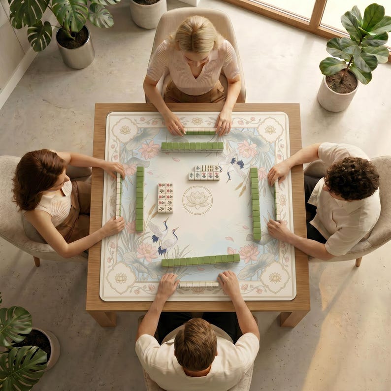 Top‑down view of four people sitting around a table covered with the crane and lotus mahjong table mat, preparing to play mahjong.