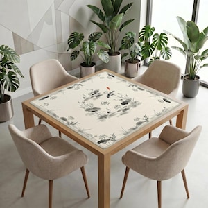Modern dining space with many green plants and neutral chairs, featuring a wooden table covered by the ink crane lotus mahjong table mat as a minimalist decorative centerpiece.