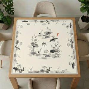 Wooden dining table with beige chairs and plants, topped with the ink crane and lotus mahjong table mat, showing the full black‑and‑white brush painting design.